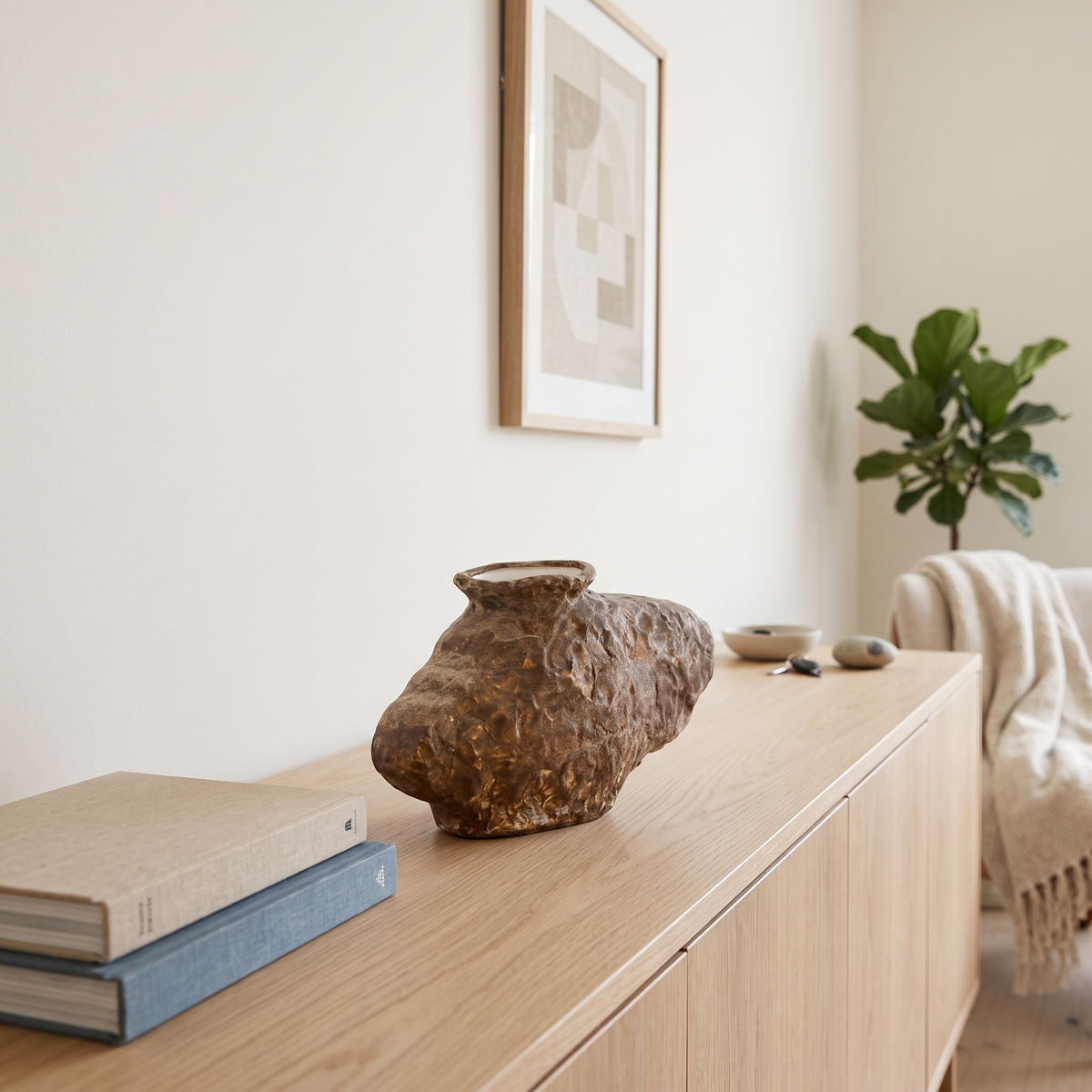 Sculptural bronze-brown porcelain vase on a pale oak console in a bright Muscat living room