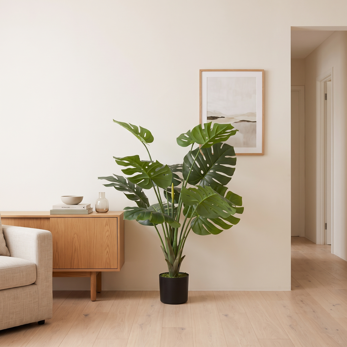Artificial Monstera plant against a warm-white wall beside an oak sideboard